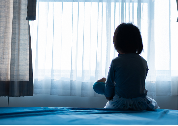 A child holding a doll and looking out of a window