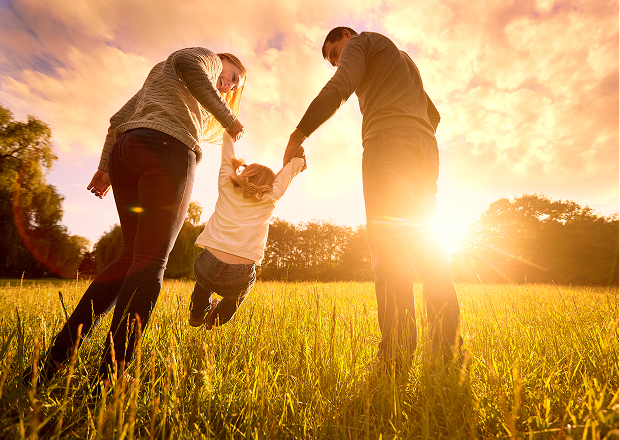 A couple swinging a child in a sunny meadow