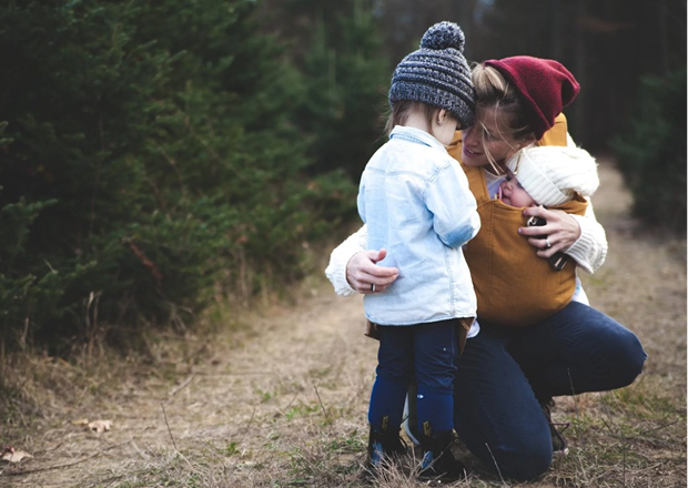 A person holding a baby in a sling while hugging another child