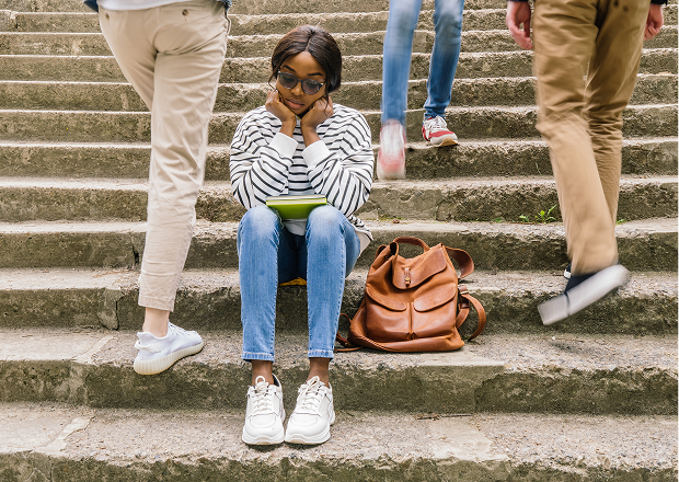 A person reading while sitting on outdoor stairs with people walking by